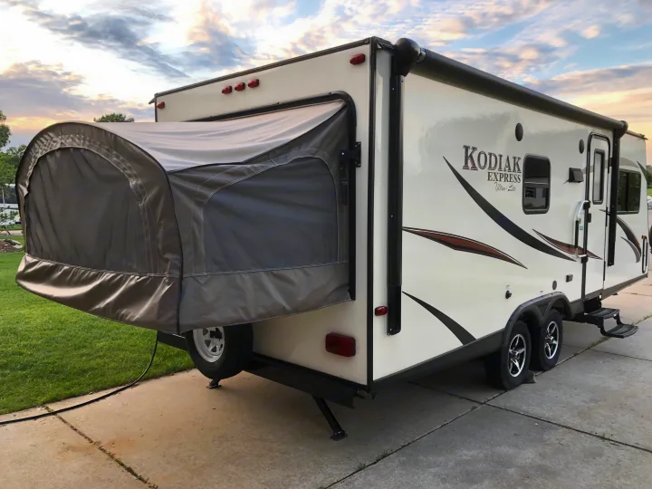 A cream-colored Kodiak Express expandable travel trailer, an excellent RV rental option, parked on concrete at dusk.. Dutchmen Kodiak 2016