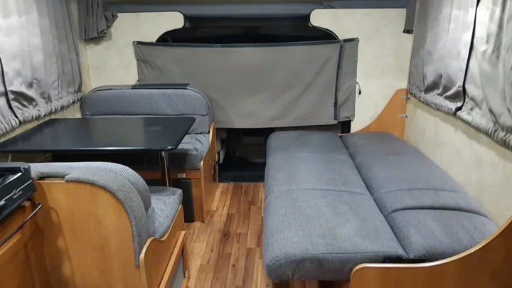 An RV rental's inviting interior showing a dinette, grey upholstered seating, a convertible bed area, and wood floors.. Majestic Leisure Craft 28A 2013