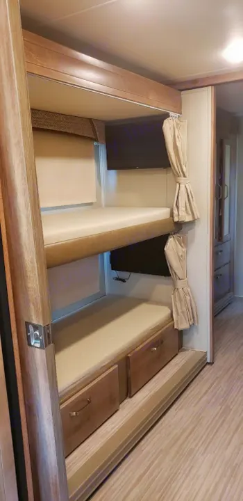 This RV rental features cozy stacked bunk beds, each with a mounted TV, window shade, and lower storage drawers. Perfect camper comfort.. Jayco Greyhawk 2019