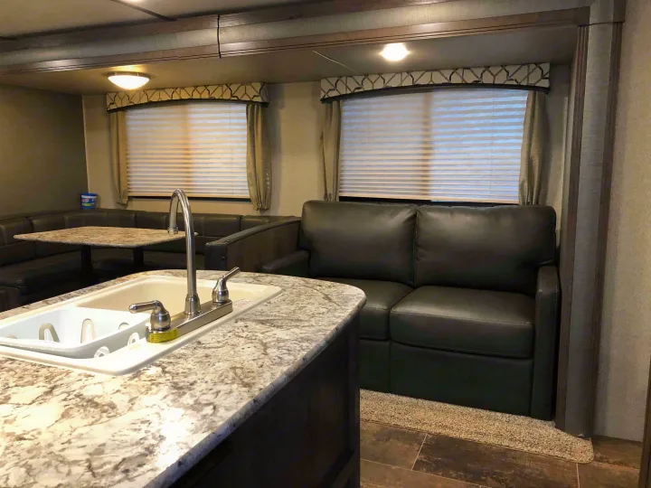 This RV rental shows a modern interior with a kitchen sink counter, dining booth, and a dark sofa for a cozy living space.. Keystone Passport 2019
