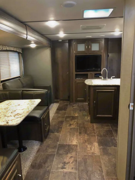 RV rental interior: living area with dinette & sofa, kitchen with sink & dark wood cabinets, modern tiled floor.. Keystone Passport 2019