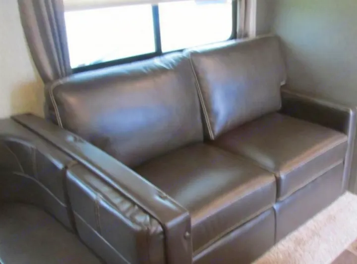 Dark brown faux leather sofa with light stitching and compact design, providing comfortable seating in this RV rental.. Keystone Passport 2019