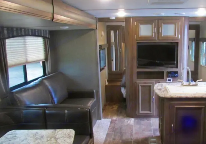 Modern rv rental interior featuring a living area with a sofa, dinette, entertainment center, and a compact kitchen with sink.. Keystone Passport 2019