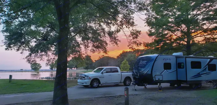 An Apex Ultra Lite RV rental & truck are perfectly set up at a tranquil lakeside campsite under a breathtaking sunset.. Coachmen Apex 265rbss 2019