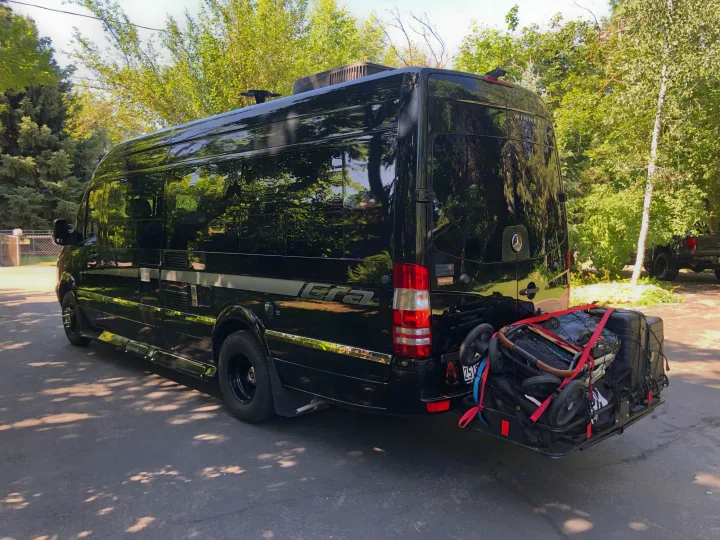 Black Winnebago Era RV rental, a sleek camper van, with a rear hitch carrier packed with a stroller and luggage.. Winnebago Era 2014