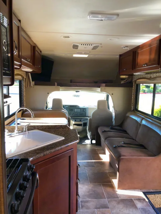 This RV rental interior showcases a kitchen, living area with sofa, cab-over bed, and front cabin. Bright & ready for travel.. Thor Motor Coach Four Winds 2015