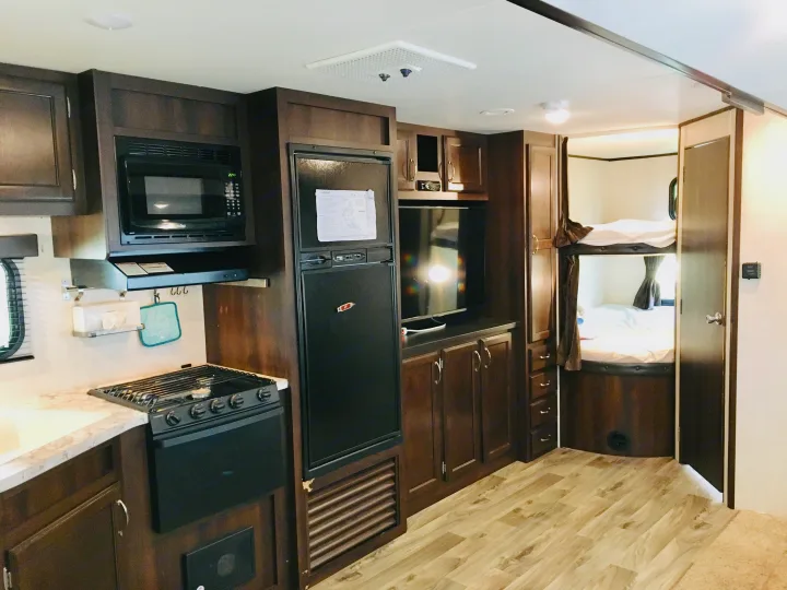Experience comfort in this RV rental's interior, showcasing a functional kitchen, entertainment center with TV, and practical bunk beds.. Jayco Jay Flight 2018