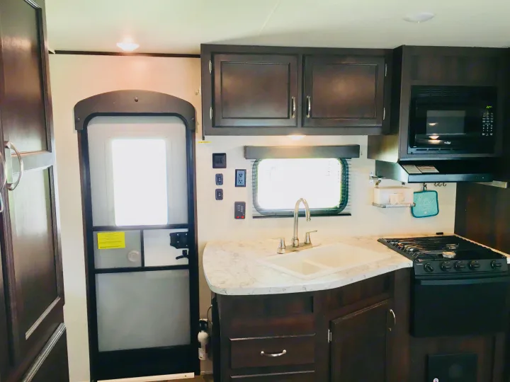 RV rental kitchen showcasing a double sink, gas stove, microwave, and dark cabinets inside a modern RV.. Jayco Jay Flight 2018