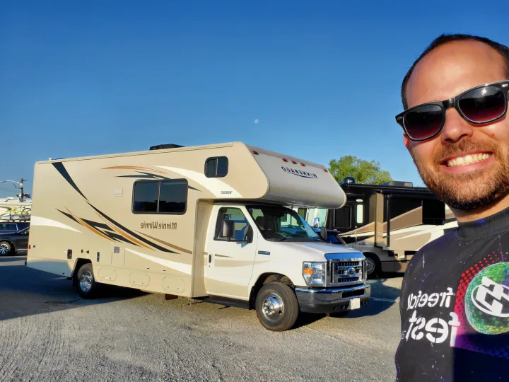 Smiling man with his Winnebago Minnie Winnie rv rental under a clear blue sky with the moon visible.. Winnebago Minnie Winnie 2018