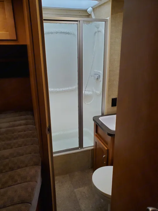 Compact RV rental bathroom with shower, sink, and toilet, next to a cozy bunk bed area, showcasing efficient space use.. Winnebago Minnie Winnie 2018