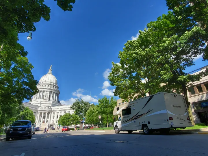 A Minnie Winnie RV rental is parked on a city street, framed by trees, with a grand state capitol building behind it.. Winnebago Minnie Winnie 2018