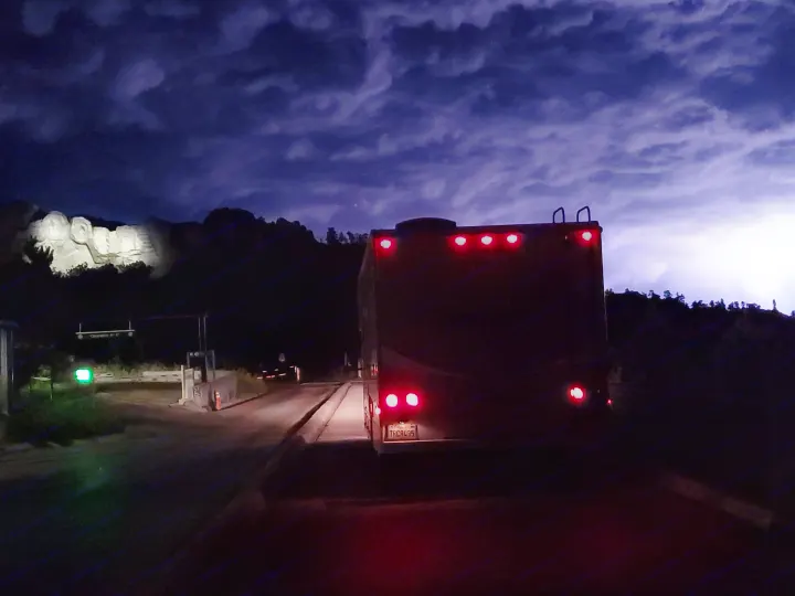 Arriving at illuminated Mount Rushmore at night in an RV rental under a storm-lit sky with lightning.. Winnebago Minnie Winnie 2018
