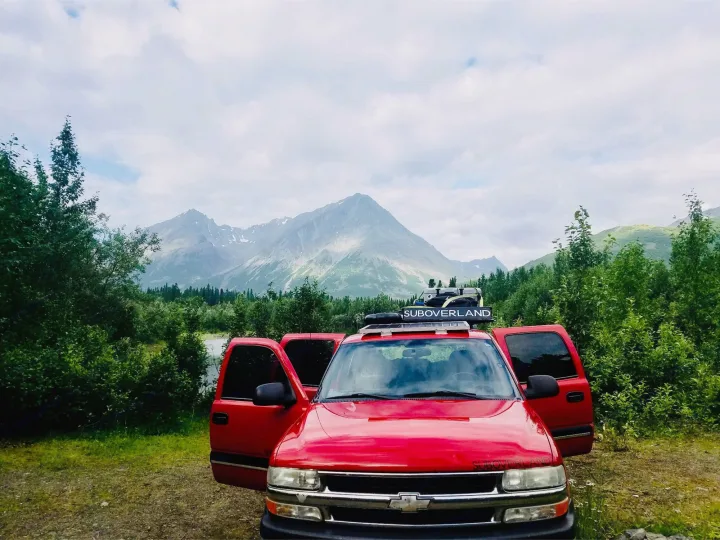 Red pickup with doors open in scenic mountains and lush greenery, a great rv rental choice for adventure.. Chevrolet Suburban Overland 2001