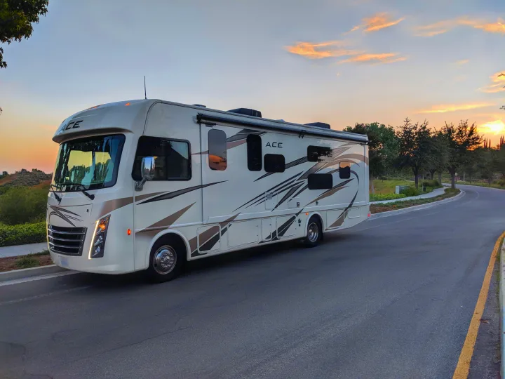 White ACE RV rental awaits adventure, bathed in soft sunset light on a peaceful road.. Thor Motor Coach A.C.E 2019