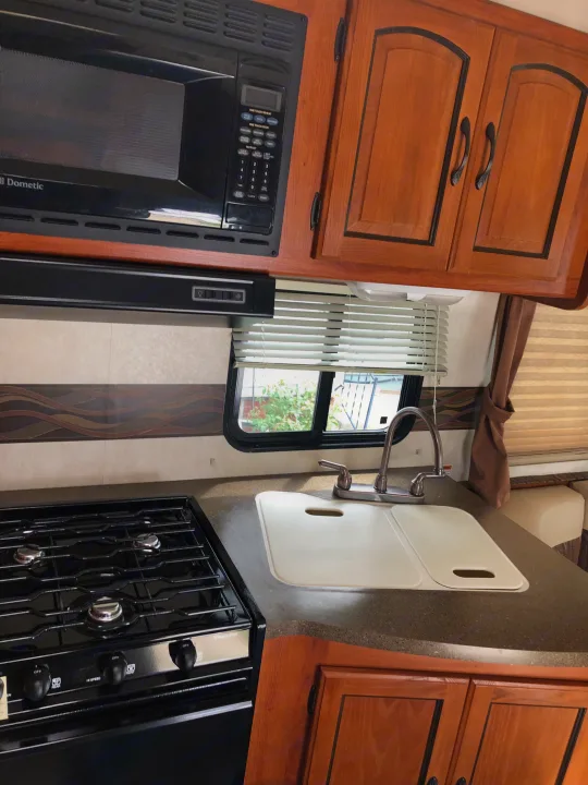 Compact RV rental kitchen with a Dometic microwave above a Magic Chef stove, alongside a sink, and wood cabinets.. Ford Coachman 2009