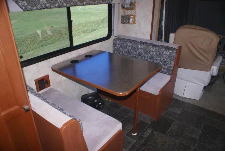 Inside an **rv rental**: a compact dinette with patterned benches, a table with cupholders, and a scenic window view.. Winnebago Vista 2013
