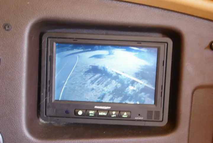 An RV rental's dashboard monitor shows a bright rear camera view of a road and terrain, with MobileVision controls below.. Winnebago Vista 2013