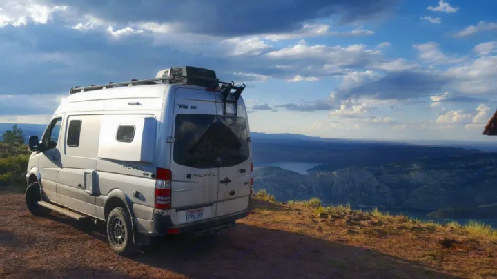 Silver Winnebago Revel rv rental parked on a hill overlooking a vast lake and mountain landscape under cloudy skies.. Winnebago Mercedes Sprinter 2019