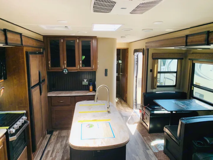Spacious RV rental interior featuring a full kitchen with island, dining area, and warm wood accents. Great for family trips.. Grand Design Reflection 2019