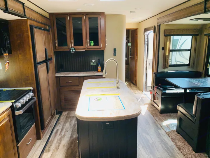 Bright RV rental kitchen and dining area with modern appliances like stove, fridge, island sink, plus a comfy booth.. Grand Design Reflection 2019
