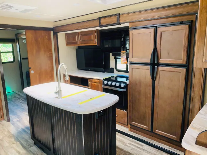 This RV rental's kitchen features an island with a sink, full-size refrigerator, oven, and microwave. Wooden cabinetry and flooring.. Grand Design Reflection 2019