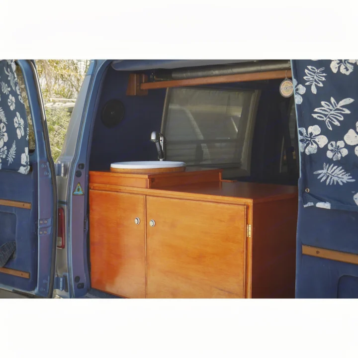 Explore this RV rental's custom van conversion: a cozy kitchen with wood cabinets, sink, and patterned blue curtains.. Chevrolet Other 1989