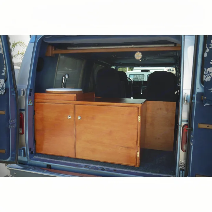 Inside an RV rental, a custom-built camper van features wooden cabinets, a sink, and blue carpet flooring.. Chevrolet Other 1989