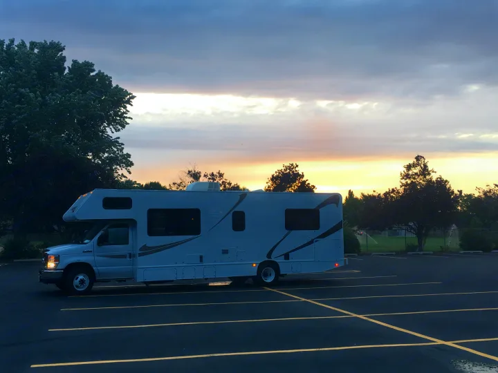 This white RV rental is parked in an empty lot at dusk/dawn, its front lights on. The sky shows warm hues, perfect for your next road trip adventure.. Majestic Leisure Craft Tourer Ii 2015