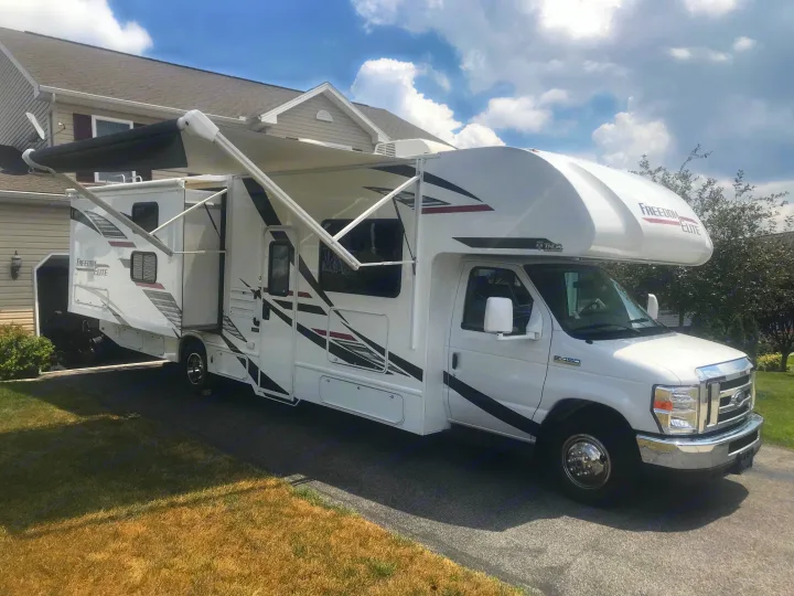White motorhome rv rental parked in a paved driveway with awnings extended, alongside a house.. Thor Freedom Elite 2020