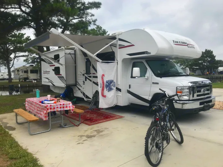 Your RV rental adventure begins here: A motorhome campsite with extended awning, picnic table, and bicycles ready for exploring.. Thor Freedom Elite 2020