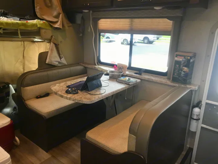 Cozy RV rental interior showing a dinette with laptop workspace, bunk bed, and window view for comfortable travel and camping.. Thor Freedom Elite 2020