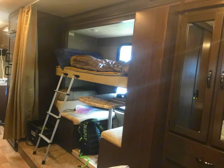 RV rental interior: A compact space with bunk beds (ladder visible), a dinette, and storage cabinets on the right.. Thor Freedom Elite 2020