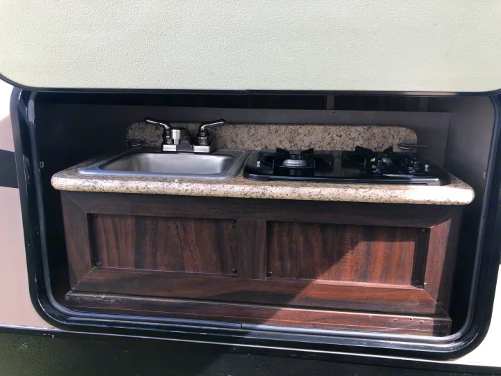 RV rental outdoor kitchen featuring a sink, two-burner stove, and granite-look countertop in an open compartment.. Pacific Coachworks Panther BHSS 2019