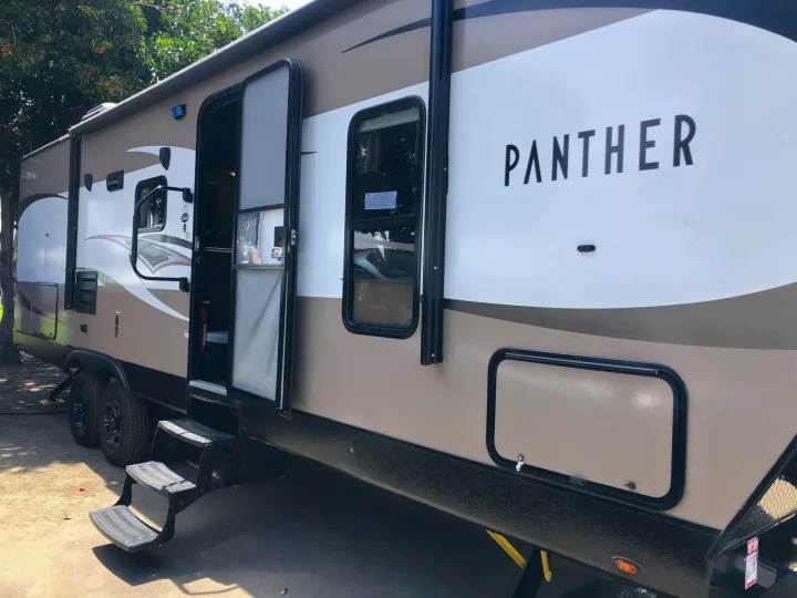 A modern, tan and white Panther RV rental, ready for adventure with its steps down and door open in an outdoor setting.. Pacific Coachworks Panther BHSS 2019