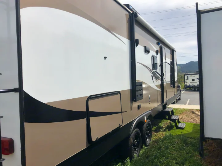 A modern travel trailer for RV rental, showcasing its side with an extended slide-out, steps, and rolled awning.. Pacific Coachworks Panther BHSS 2019