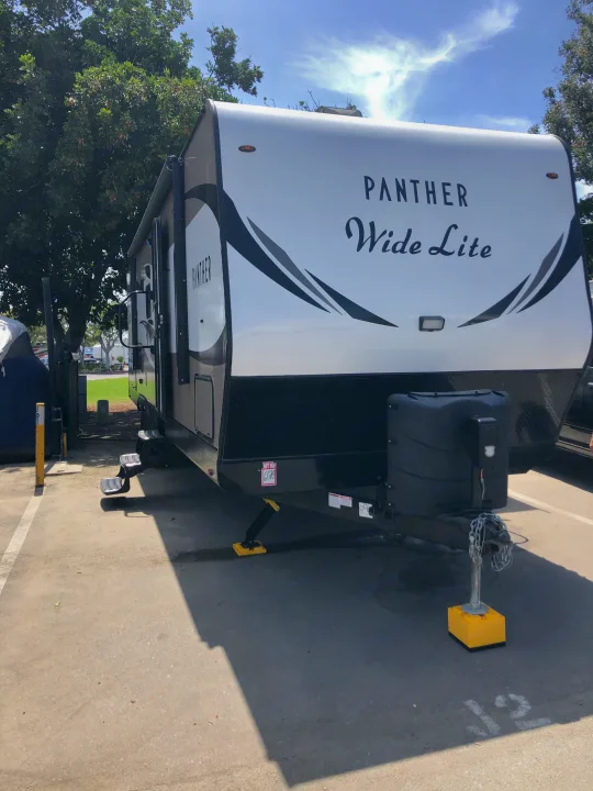 White "Panther Wide Lite" RV rental parked at sunny outdoor site 12 with steps down & stabilizers set.. Pacific Coachworks Panther BHSS 2019