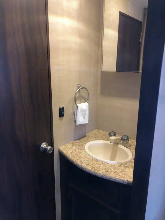 RV rental: Compact bathroom with dark wood door on left, light vanity with oval sink, and mirror above.. Pacific Coachworks Panther BHSS 2019