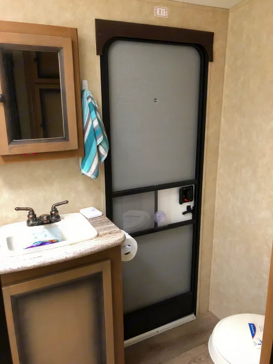 RV rental bathroom features a compact sink, mirror, and toilet. A screen door with an 'EXIT' sign provides access.. Cruiser Rv Corp Radiance 2014