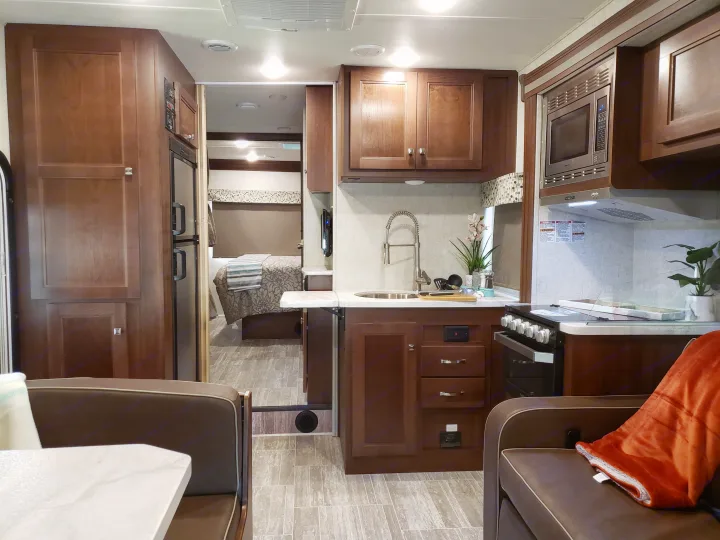 Spacious RV rental interior featuring a full kitchen with dark wood cabinetry, a comfortable living area, and a bedroom beyond.. Other Other 2019