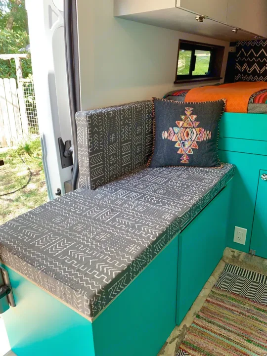 Cozy RV rental interior with a patterned bench, colorful accent pillow, and teal storage, offering a view outside.. Dodge 2500 Promaster 2019