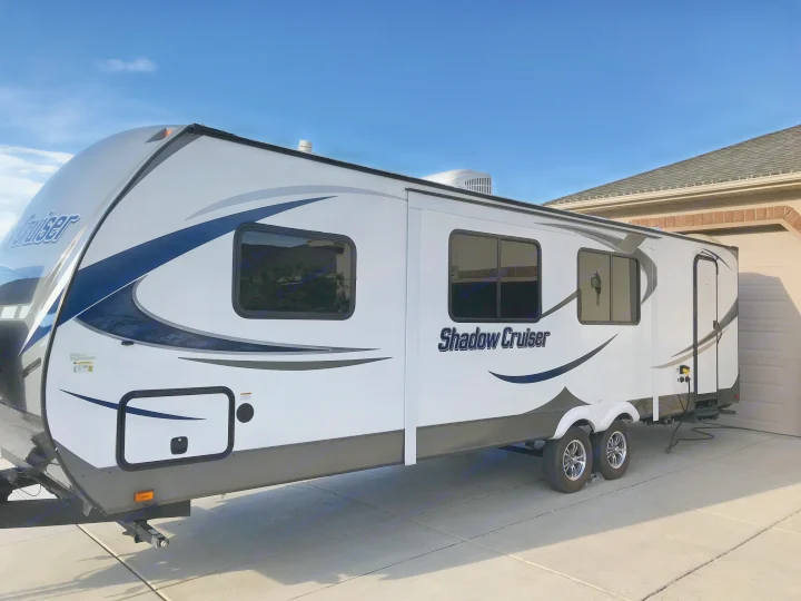 A white Shadow Cruiser travel trailer, ideal for RV rental, parked on a sunny day. This spacious RV has dark windows and blue/gray accents.. Cruiser RV Shadow Cruiser 2015