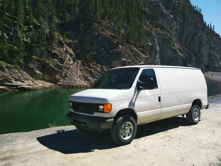 White cargo van (like an rv rental) by a deep green lake and forested mountain on a sunny day.. Ford Econoline 2006