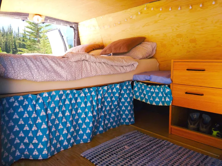 Cozy RV rental interior with a comfy bed, wooden walls, unique teepee-patterned storage curtains, and forest views.. Ford Econoline 2006