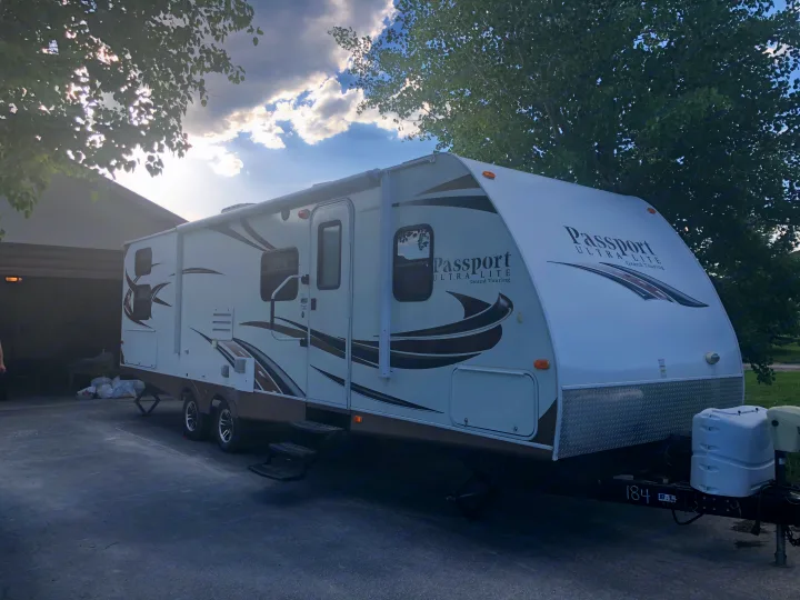 A white and brown Passport travel trailer, looking like an ideal RV rental, is parked on a paved driveway in daylight.. Keystone Passport 2014