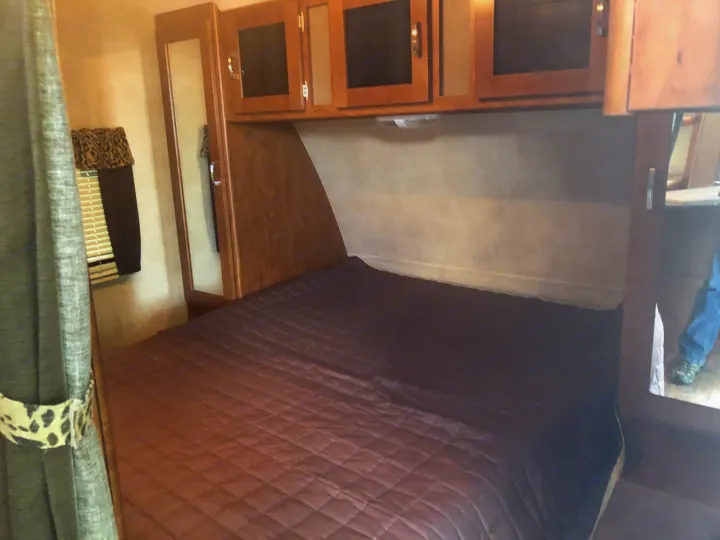 An inviting RV rental bedroom with a quilted bed, ample overhead storage, and a mirrored wardrobe for convenience.. Keystone Passport 2014