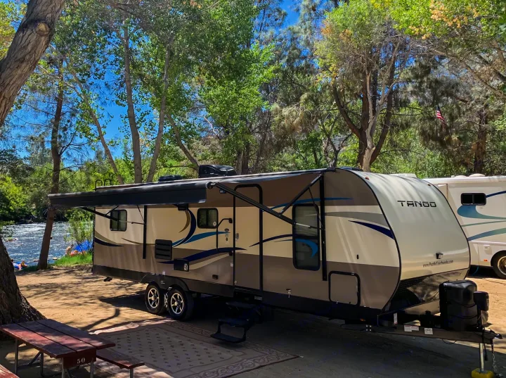 Riverside RV rental: Tango travel trailer at a shaded campsite by the water with an awning extended, perfect for outdoor fun.. Pacific Coachworks Tango 2020