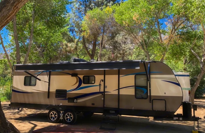 RV rental: A modern travel trailer is parked at a sunny, tree-filled campsite, ready for your outdoor adventure.. Pacific Coachworks Tango 2020