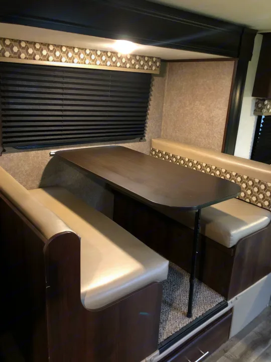 Inside an RV rental: a bright dinette area with a dark table, opposing cushioned benches, and patterned decor.. Jayco Other 2020