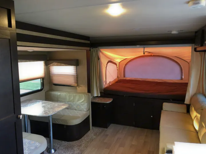 Bright RV rental interior featuring a large pop-out bed, a dinette with table, and a sofa. Ideal for comfortable travel.. Dutchmen Kodiak 2016