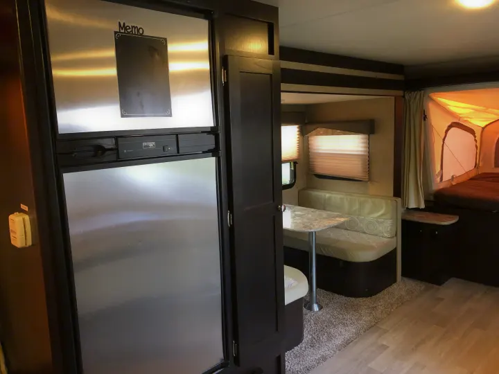 RV rental interior showcasing a stainless steel fridge, comfortable dinette, and cozy pop-out bed area.. Dutchmen Kodiak 2016